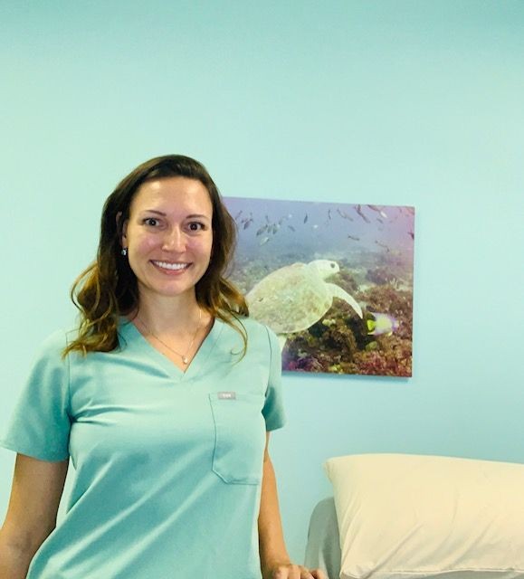 a person wearing scrubs next to a massage table with turtle picture on wall a person wearing scrubs next to a massage table with turtle picture on wall